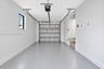 Interior garage featuring smooth white walls, a finished epoxy floor, an automatic overhead door opener, a small rectangular side window, and an inter