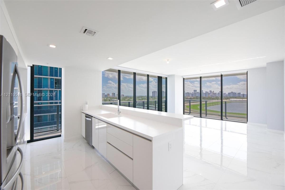 Modern kitchen featuring white flat-panel cabinetry, quartz countertops, a stainless steel dishwasher, stone-finish tile flooring, and floor-to-ceilin