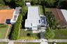 Aerial view of a flat-roof residence featuring a paved walkway, manicured lawn, established landscaping, and an enclosed storage structure