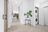 Neutral-tone tile flooring, sliding wood-finish barn door with matte black hardware, and laundry alcove featuring stacked appliances and louvered fold