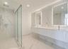 Floating dual-sink vanity with under-cabinet lighting, floor-to-ceiling stone-tiled walls, glass-enclosed walk-in shower, recessed ceiling lighting, a