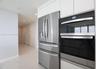 Stainless steel French door refrigerator and stacked double oven, complemented by white flat-panel cabinetry and large-format tile flooring