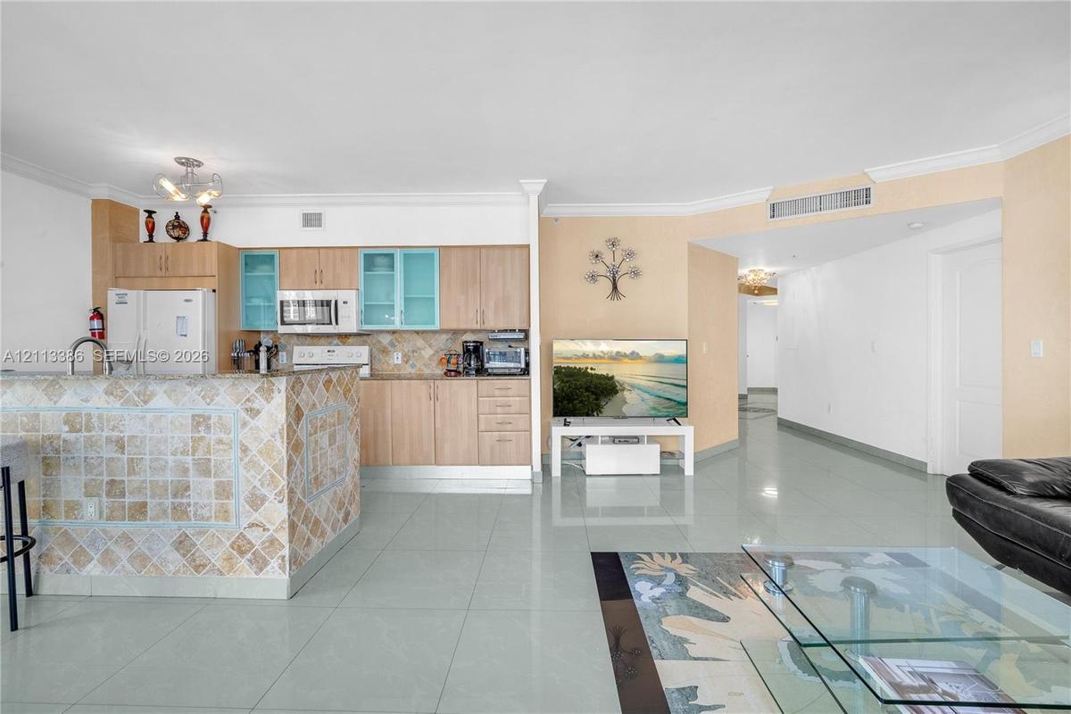 Open-concept kitchen featuring wood-finish cabinetry, a tile-faced breakfast bar, and large-format tile flooring throughout the living area