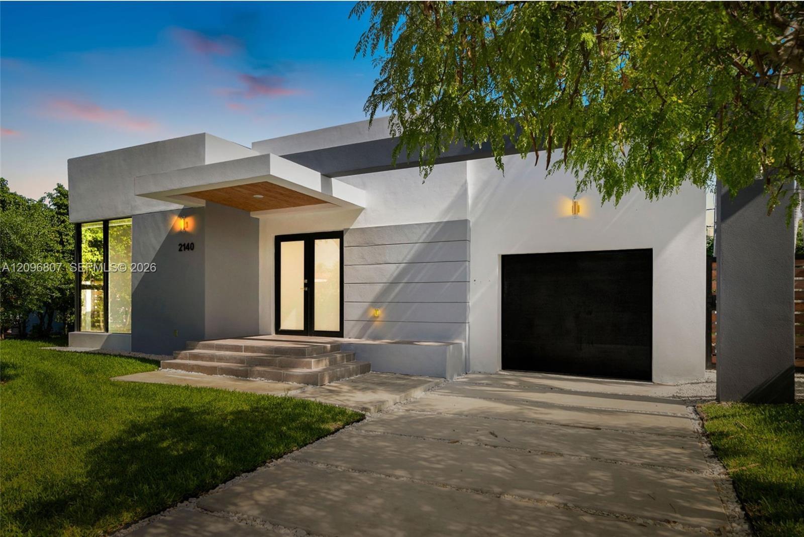 Modern exterior featuring a smooth stucco facade, dual-tone architectural detailing, a covered entrance with wood-paneled ceiling, and a concrete driv