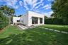 Modern exterior featuring smooth white stucco finish, built-in hot tub, concrete paver pathways, manicured lawn, and perimeter privacy hedges