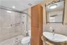 Walk-in shower with sliding glass enclosure and tiled walls, stone-finish countertop with vessel sink, tall built-in wooden cabinetry, and decorative 