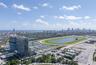 Aerial perspective featuring a multi-story glass-facade residential building, a large-scale race track, and a coastal skyline backdrop