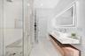 Floating dual-sink vanity with wood-finish cabinetry, quartz countertops, frameless glass walk-in shower with decorative tile accents, and an integrat