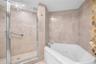 Glass-enclosed shower with metal grab bar, jetted corner tub, and neutral stone tile surround