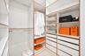 Custom walk-in closet featuring floor-to-ceiling white shelving with wood-tone edging, multiple integrated drawers, and dual-level metal hanging rods