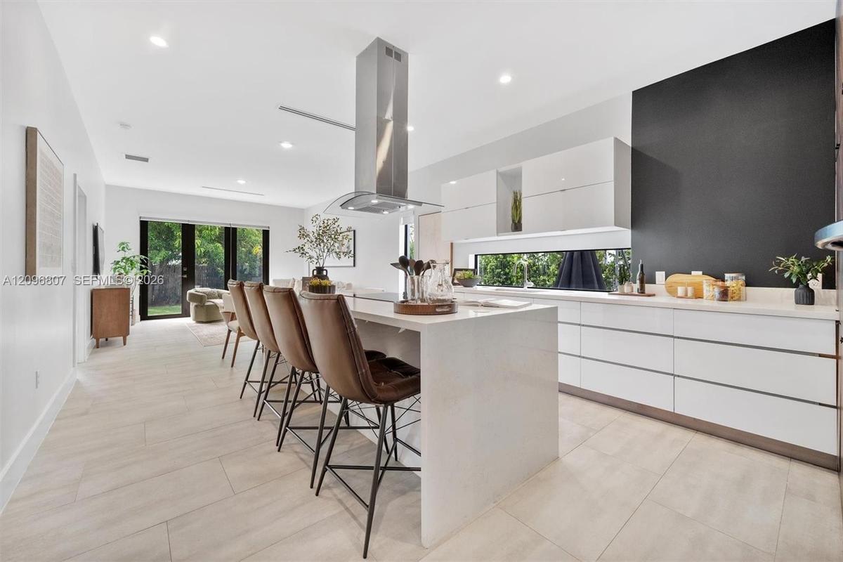 Kitchen featuring a large central island with quartz countertops, minimalist high-gloss white cabinetry, a stainless steel chimney-style range hood, a