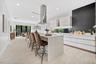 Kitchen featuring a large central island with quartz countertops, minimalist high-gloss white cabinetry, a stainless steel chimney-style range hood, a