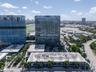 Aerial perspective of high-rise glass-facade towers featuring structured parking facilities with geometric roof patterns and integrated palm tree land
