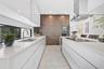 Modern kitchen featuring flat-panel white cabinetry, expansive stone countertops, geometric-patterned wall paneling, built-in stainless steel applianc