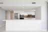 Modern kitchen featuring high-gloss white cabinetry, expansive stone-finish peninsula, stainless steel french-door refrigerator, integrated double ove