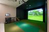 Golf simulator room featuring a large-scale projection screen, synthetic turf flooring, sound-dampening wall panels, and ceiling-mounted projection ha