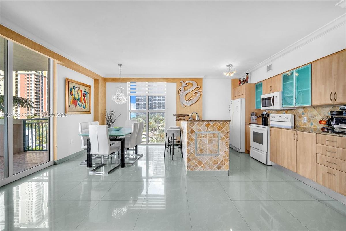 Open-concept area featuring light wood-finish cabinetry, tile-clad kitchen island, polished tile flooring, glass-paneled upper cabinets, and floor-to-