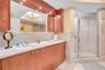 Dual-sink vanity with stone countertop, wood cabinetry, large recessed mirror, and glass-enclosed shower with tiled surround