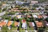 Aerial perspective of residential property featuring a flat roof structure, grass lawn, and dense perimeter landscaping