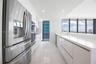 Modern kitchen featuring high-gloss white cabinetry, expansive stone countertops, stainless steel appliances, floor-to-ceiling windows, and large-form