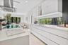 Contemporary kitchen featuring flat-panel high-gloss cabinetry, stone-surface countertops, a full-width horizontal backsplash window, a stainless stee