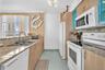 Kitchen featuring light wood-finish cabinetry, stone-surface countertops, dual-basin stainless steel sink, tile flooring, and integrated white applian