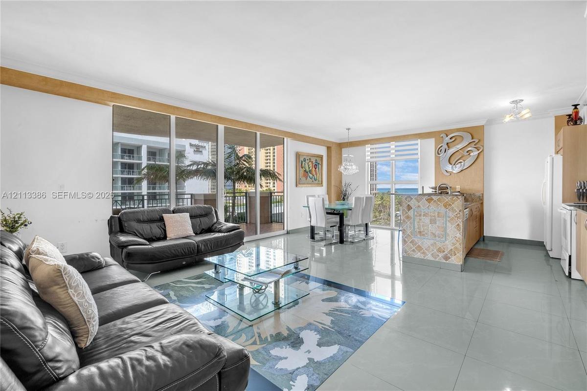 Open-concept living area featuring large-format tile flooring, floor-to-ceiling glass sliding doors, and a kitchen island with stone tile cladding