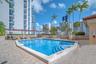 Swimming pool featuring a stone-paver deck, pergola-style covering, and palm tree landscaping