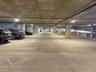 Covered parking garage featuring reinforced concrete construction, support pillars, overhead lighting, and designated parking stalls