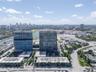 Aerial perspective of high-rise structures featuring glass curtain wall construction and expansive paved parking areas
