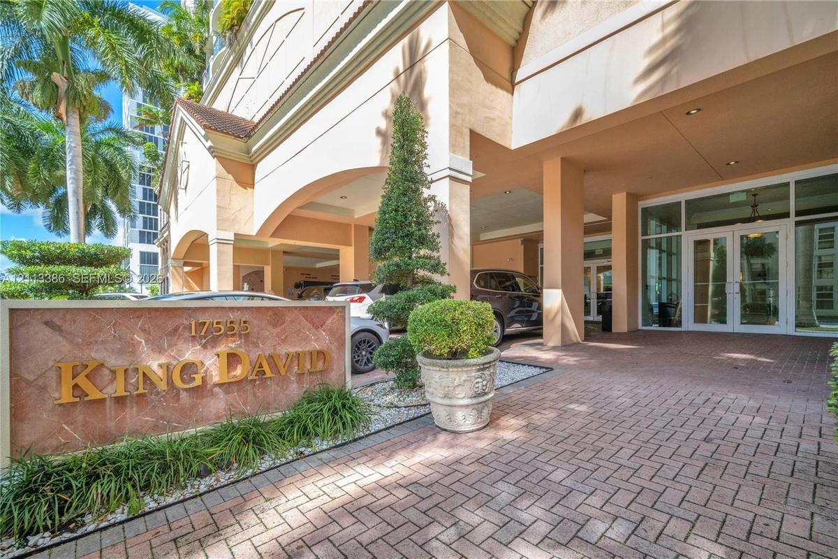 Covered porte-cochère entry featuring a red brick paver driveway, natural stone monument signage, and structured landscape elements
