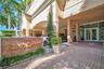 Covered porte-cochère entry featuring a red brick paver driveway, natural stone monument signage, and structured landscape elements