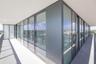 Wrap-around exterior balcony featuring floor-to-ceiling glass panels, dark metal framing, concrete flooring, and minimalist railing