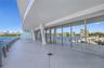 Expansive wraparound balcony featuring large-format tile flooring, a glass railing system, structural architectural pillars, and floor-to-ceiling glas