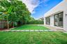 Exterior space featuring a concrete patio, synthetic turf lawn, stone paver pathway, and dual glass-paneled double doors