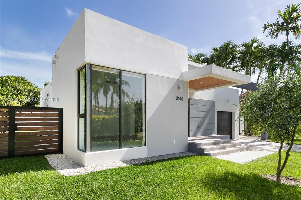 Modern exterior featuring a smooth stucco finish, floor-to-ceiling corner glazing, a wood-paneled cantilevered entryway, horizontal slat fencing, and 