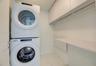 Laundry area featuring stacked white washer and dryer, white cabinetry, integrated shelving, and white tile flooring
