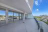 Expansive covered terrace featuring large-format tile flooring, floor-to-ceiling glass sliding doors, and a transparent glass railing system
