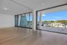 Floor-to-ceiling retractable glass walls, wide-plank wood-finish flooring, recessed lighting, and expansive covered balcony with tile surfacing