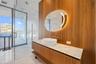 Floating wood-finish vanity with a stone-top surface and vessel sink, illuminated oval mirror, floor-to-ceiling glass-enclosed shower, and polished st