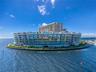 Waterfront multi-story residential complex featuring glass-railed balconies, a perimeter seawall, integrated landscaping, and a surrounding marina