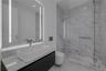 Floating vanity with integrated countertop, rectangular vessel sink, wall-to-wall mirror with vertical integrated lighting, glass-enclosed shower, and
