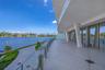 Expansive covered balcony featuring large-format tile flooring, structural support columns, full-height glass sliding doors, and a frameless glass rai