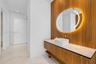 Floating wood-finish vanity with a stone countertop, white vessel sink, wall-mounted faucet, and custom wood-paneled wall featuring an integrated circ