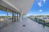 Expansive covered terrace featuring large-format tile flooring, structural support columns, floor-to-ceiling glass wall panels, and a frameless glass 