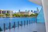 Covered balcony featuring large-format tile flooring and a transparent glass railing with vertical metal supports, overlooking a waterway