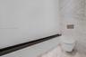 Wall-mounted toilet with a dual-flush actuator, floor-to-ceiling stone-patterned tile wall, and a horizontal dark metal accent trim