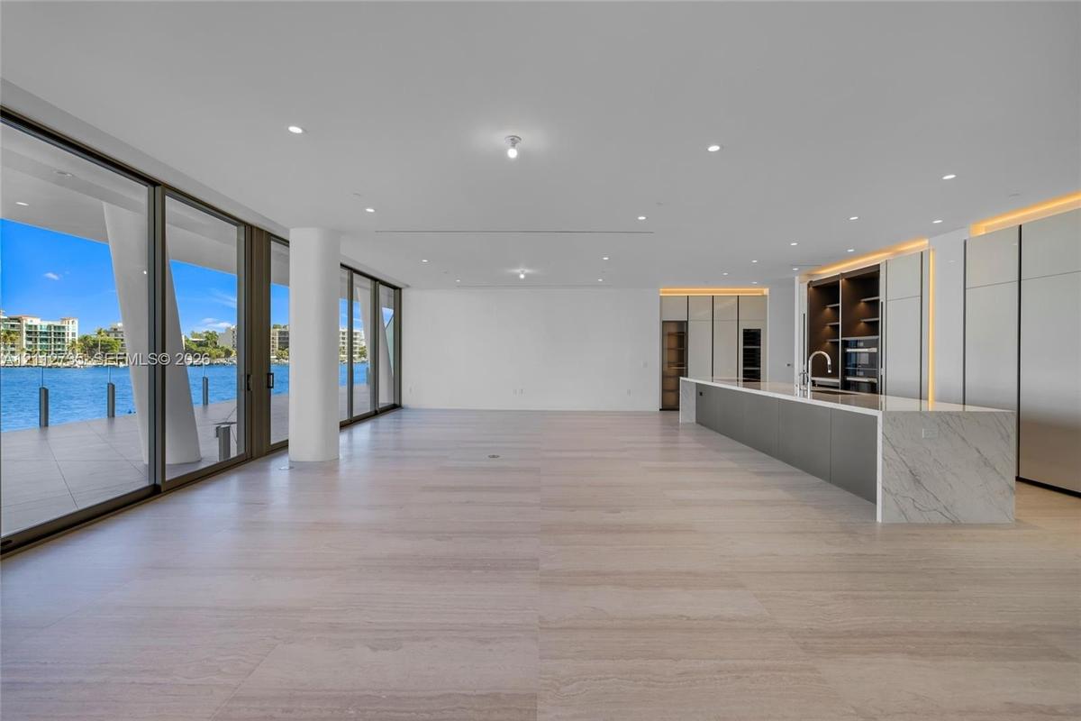 Open-concept interior featuring light-toned stone-finish flooring, floor-to-ceiling glass sliding doors, recessed lighting, and a kitchen island with 