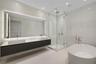 Floating double-vanity with vessel sinks, expansive LED-backlit mirror, glass-enclosed walk-in shower, and freestanding soaking tub