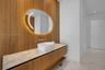 Floating wood-finish vanity with a stone countertop, white vessel sink, wall-mounted faucet, and oval backlit mirror set against a floor-to-ceiling wo